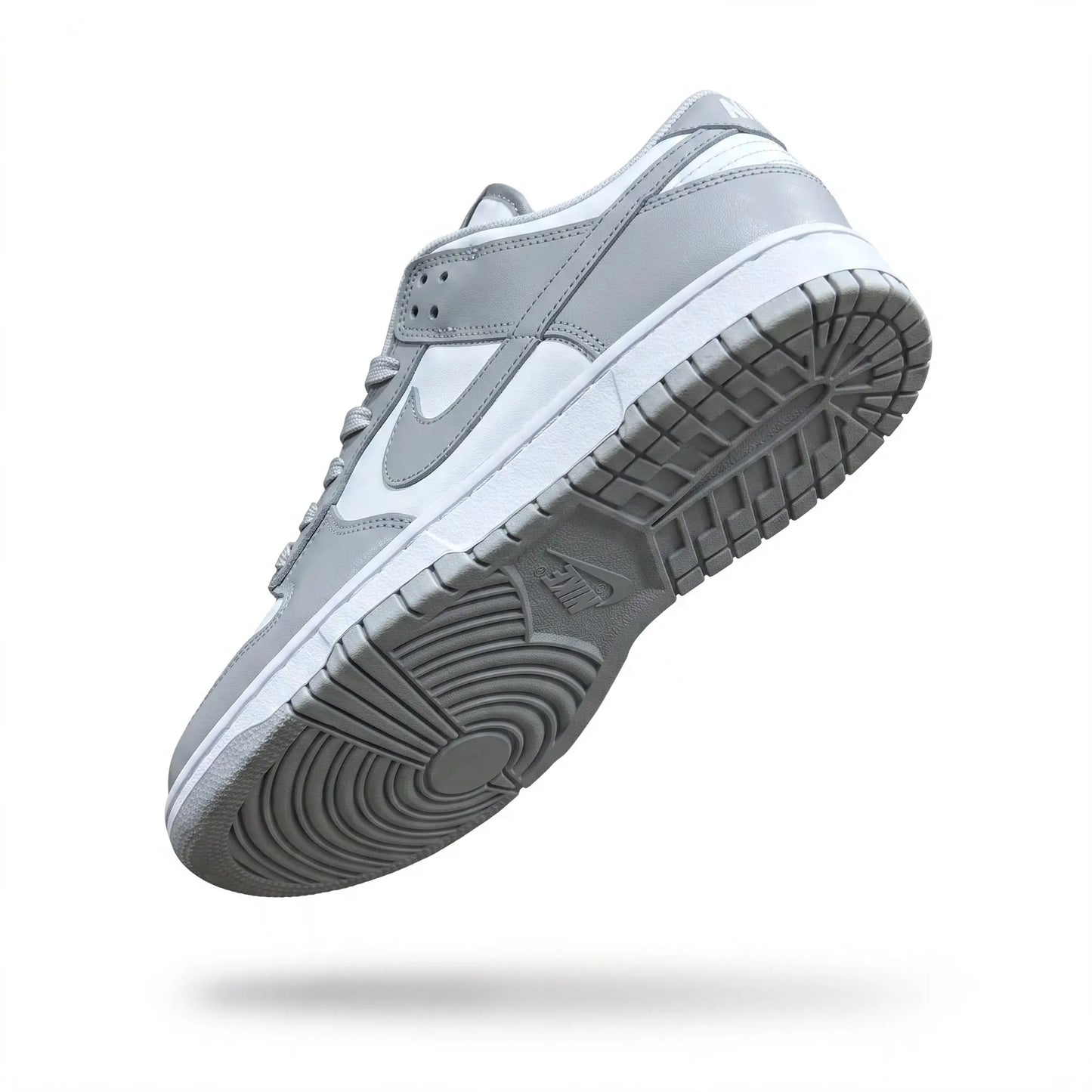 A Nike low-top sneaker shown floating at an angle, featuring a light gray leather upper, white midsole, and a textured dark gray outsole.