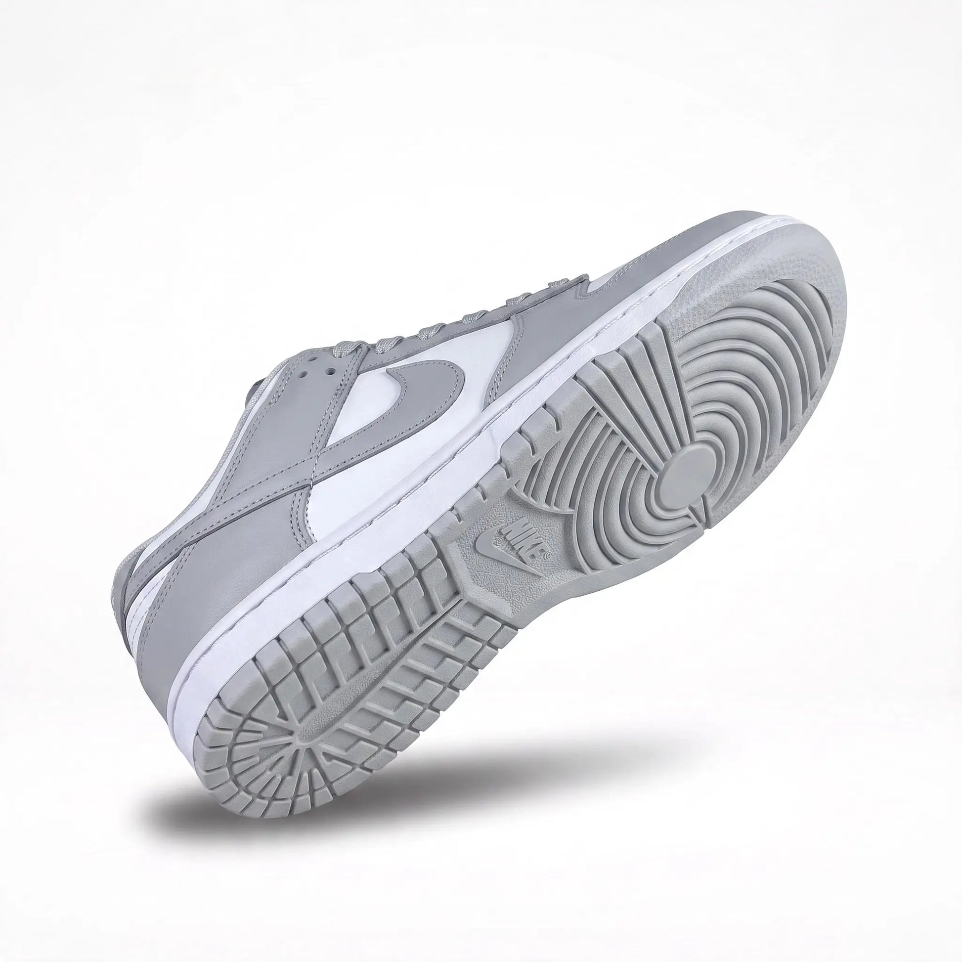 A Nike low-top sneaker shown from a side angle, featuring a light gray suede upper with a white leather Swoosh and a white midsole, set against a clean white background.