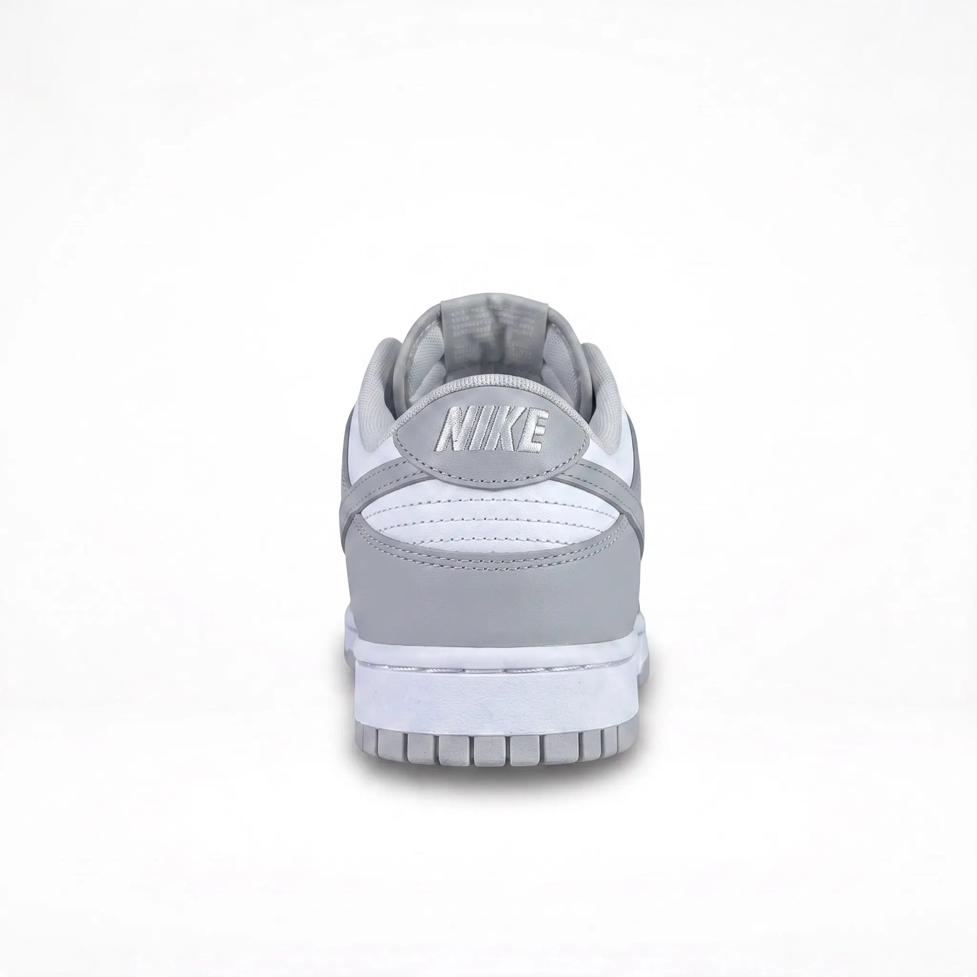 A Nike low-top sneaker shown from the back, featuring a light gray leather upper, white midsole, and a gray Nike logo on the heel tab, set against a plain white background.