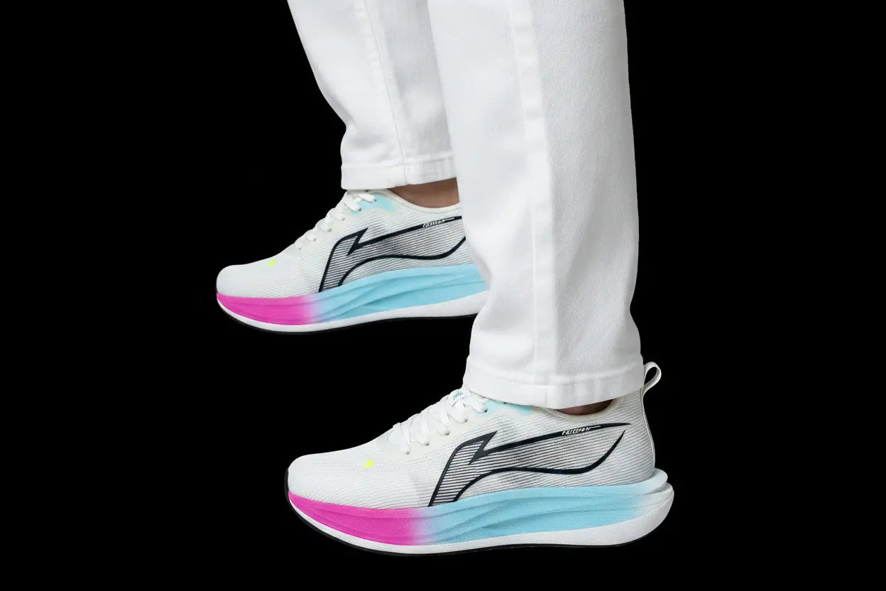 White athletic sneakers with a black and gray side logo, featuring a light blue and pink gradient midsole, shown on a person wearing white pants against a black background.