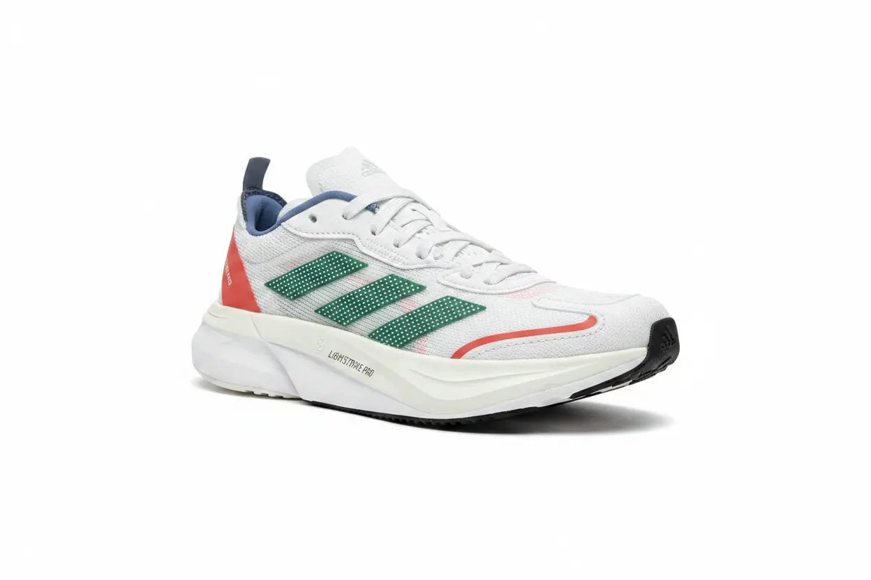 A white Adidas running shoe with green three-stripes, a coral-red heel accent, and a navy blue tongue pull tab, shown from a side profile on a white background.