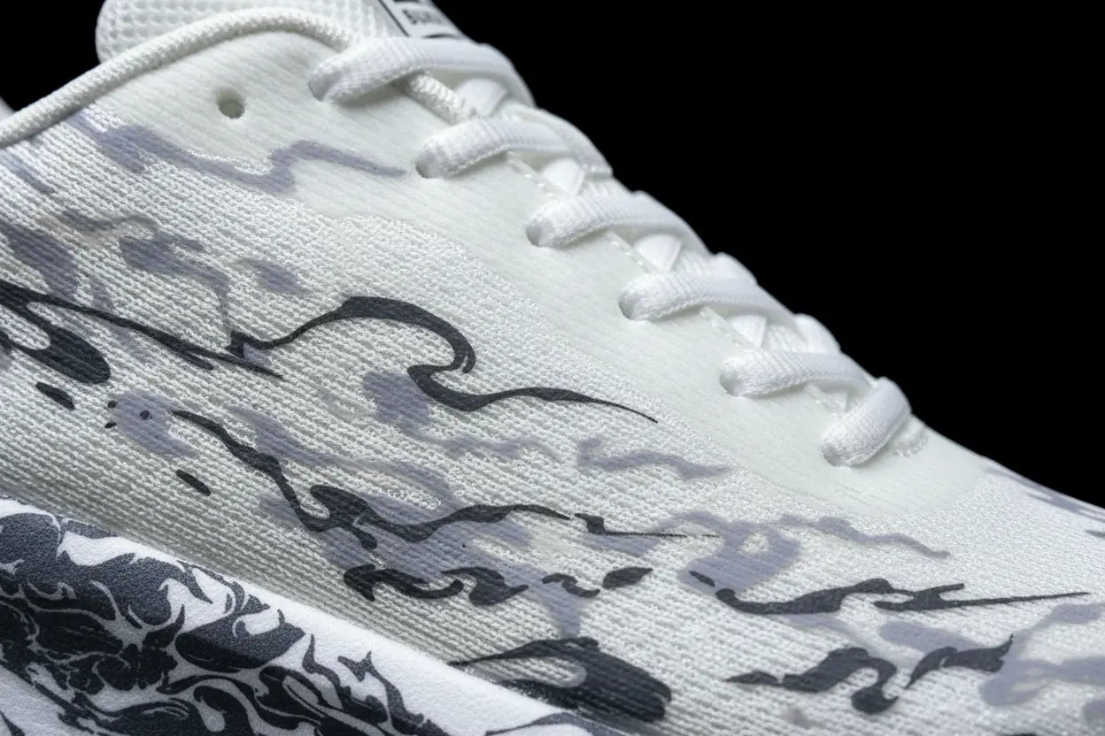 Close-up of a white athletic shoe with gray and black abstract wave-like patterns on the side, white laces, and a black background.