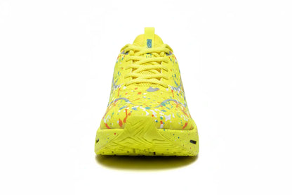 A bright yellow athletic sneaker with a colorful paint splatter pattern on the upper, shown from a front-facing perspective on a white background.