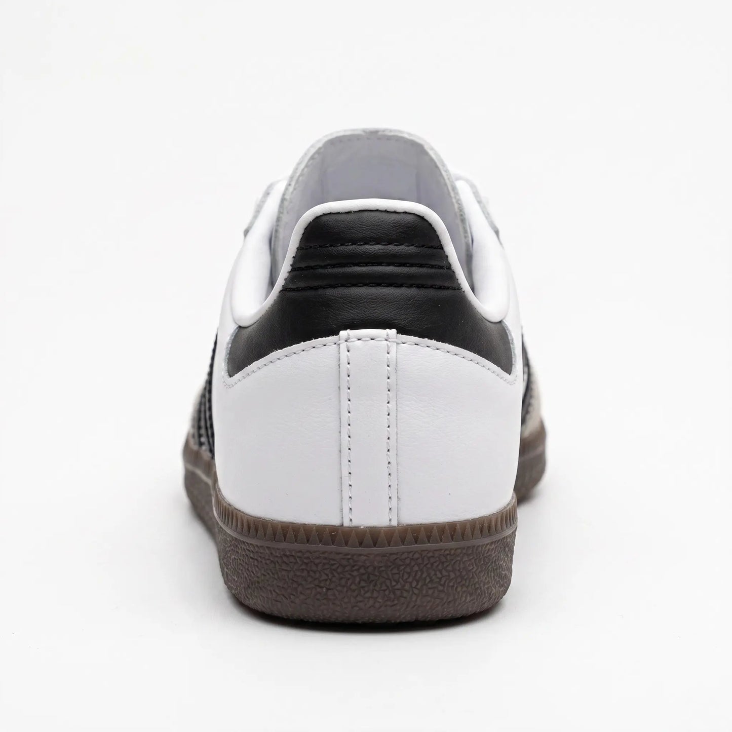 A low-top sneaker shown from the rear, featuring a white leather upper with a black leather heel tab, white laces, and a dark brown textured rubber sole.