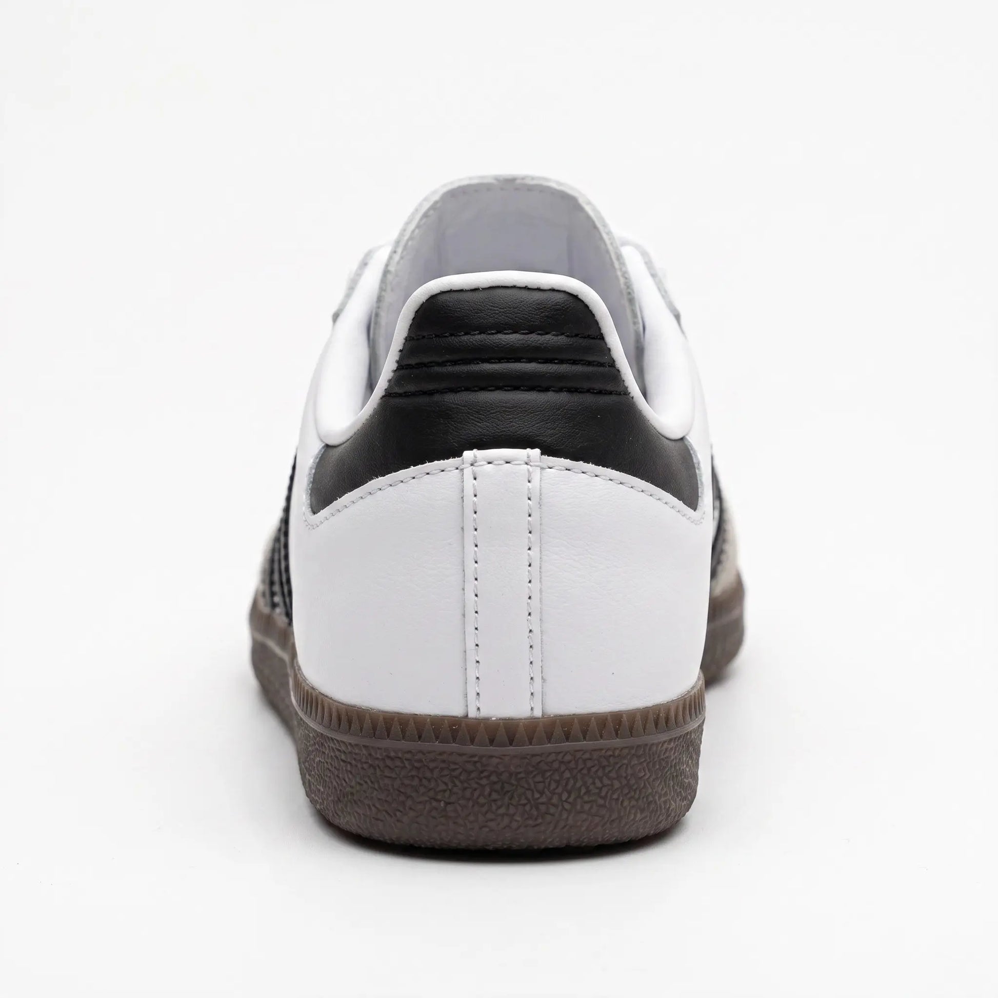 A low-top sneaker shown from the rear, featuring a white leather upper with a black leather heel tab, white laces, and a dark brown textured rubber sole.