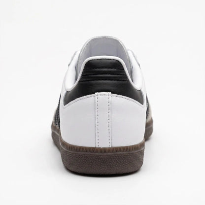 A low-top sneaker shown from the rear, featuring a white leather upper with a black leather heel tab, white laces, and a dark brown textured rubber sole.